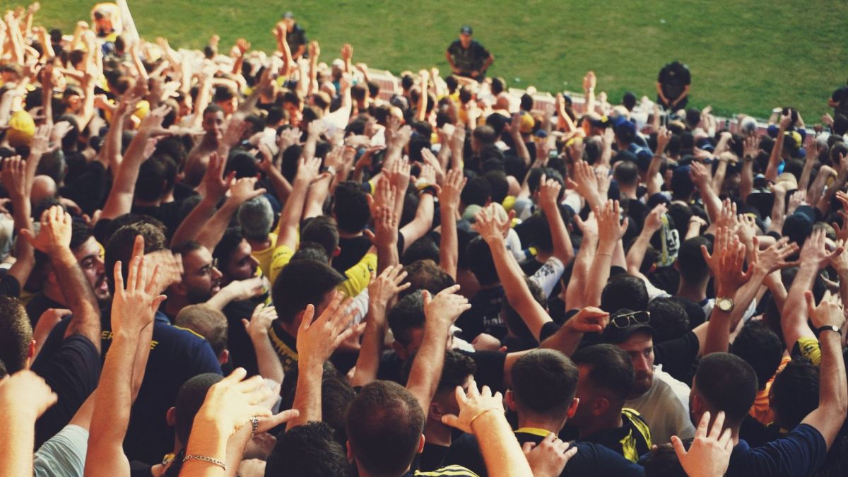 Excited crowd with raised hands at a vibrant outdoor sports event.