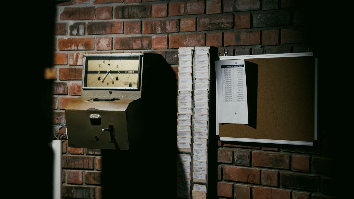 A retro time clock and stack of punch cards against a dark brick wall in an industrial setting.