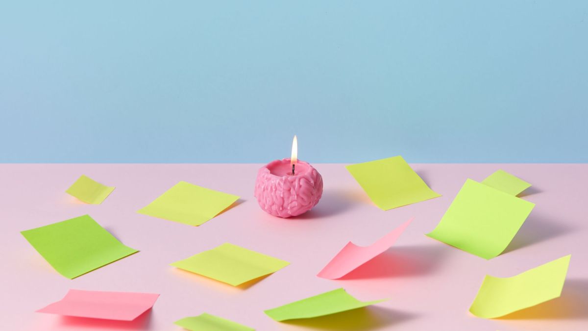 A pink brain candle lit among colorful sticky notes on pastel background, evoking creativity.