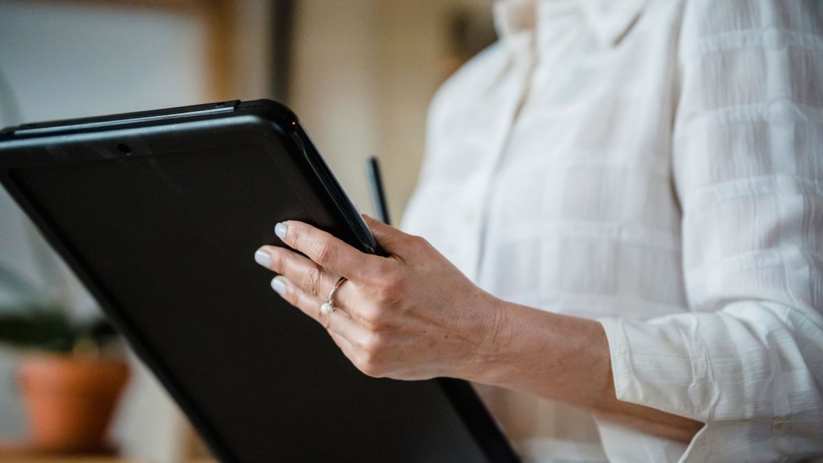 Close-up of a woman holding a digital tablet in an office environment, focusing on hand details.