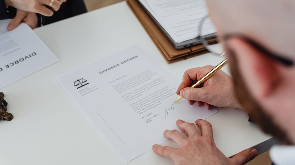 Close-up of a person signing a divorce decree on a desk.