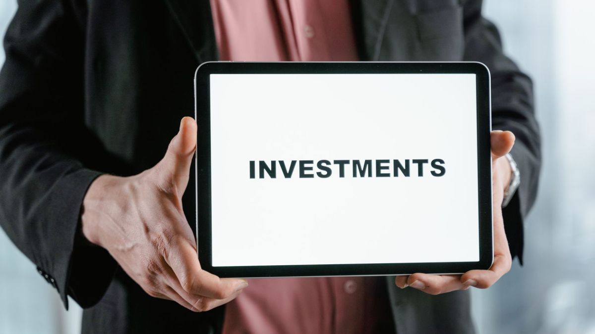 A businessman in a suit holds a tablet displaying the text 'INVESTMENTS'.
