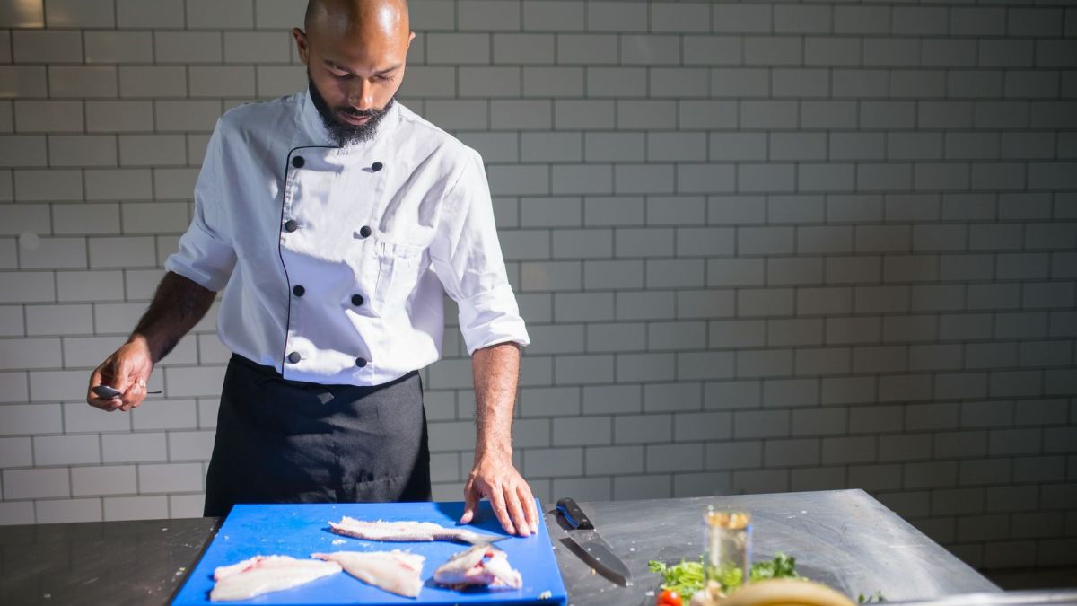 Chef in restaurant kitchen filleting fish on cutting board, focusing on culinary skills.