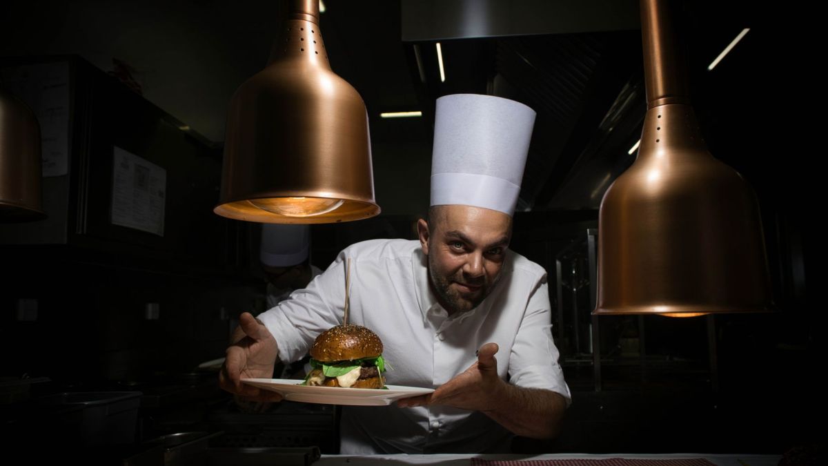 Professional chef showcasing a gourmet burger under warm kitchen lights.