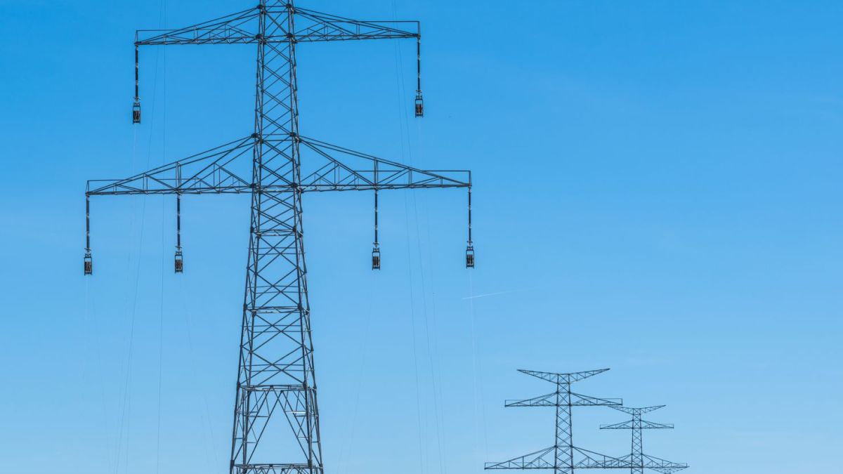 Blue sky over transmission towers on a rural landscape, symbolizing energy distribution.