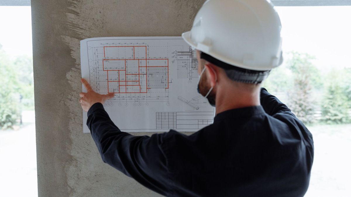 Engineer in hardhat reviewing architectural floor plans at construction site.