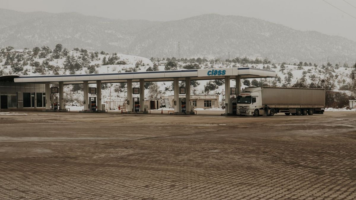 A snowy gas station with a truck and mountains in the backdrop, offering a serene winter scene.