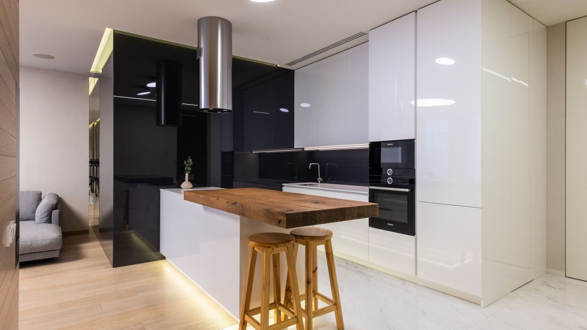 Interior of modern apartment with kitchen zone furnished with glossy cabinets and living area with sofa