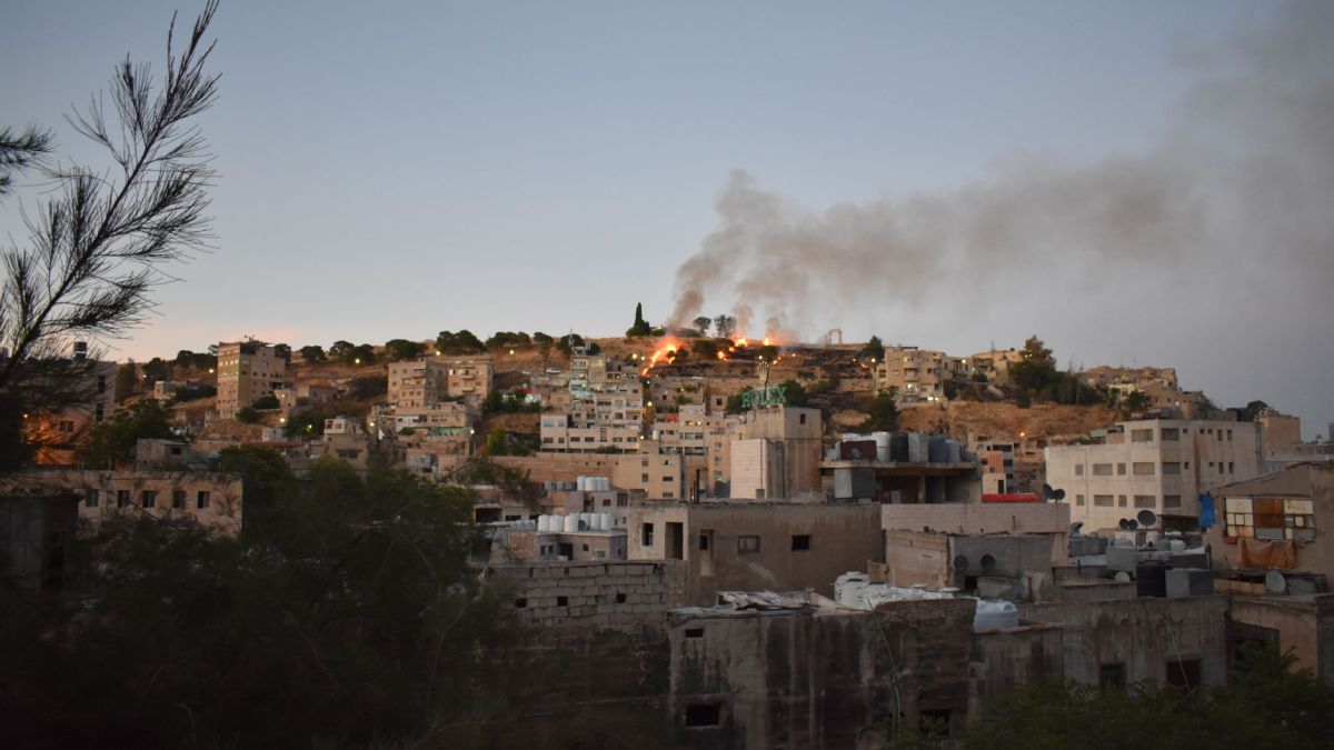 Stunning view of Amman's hilltop buildings with smoke rising, capturing a dramatic sunset cityscape.
