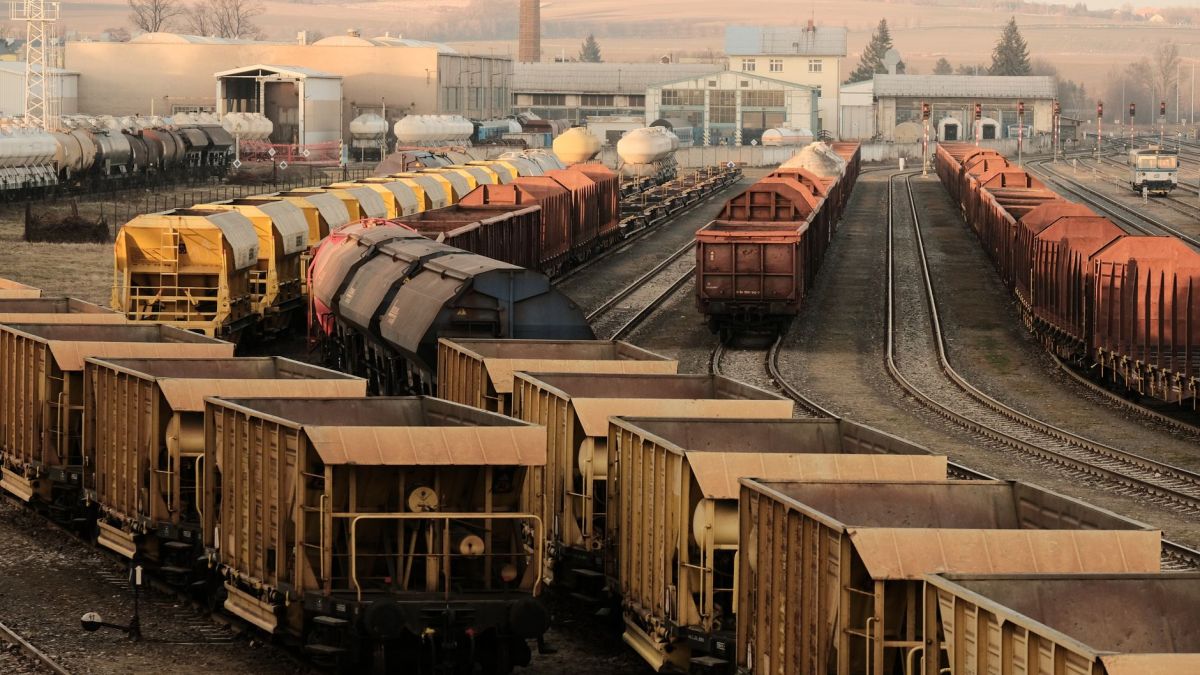 A busy freight train yard with multiple tracks and a variety of train cars in a rural setting.
