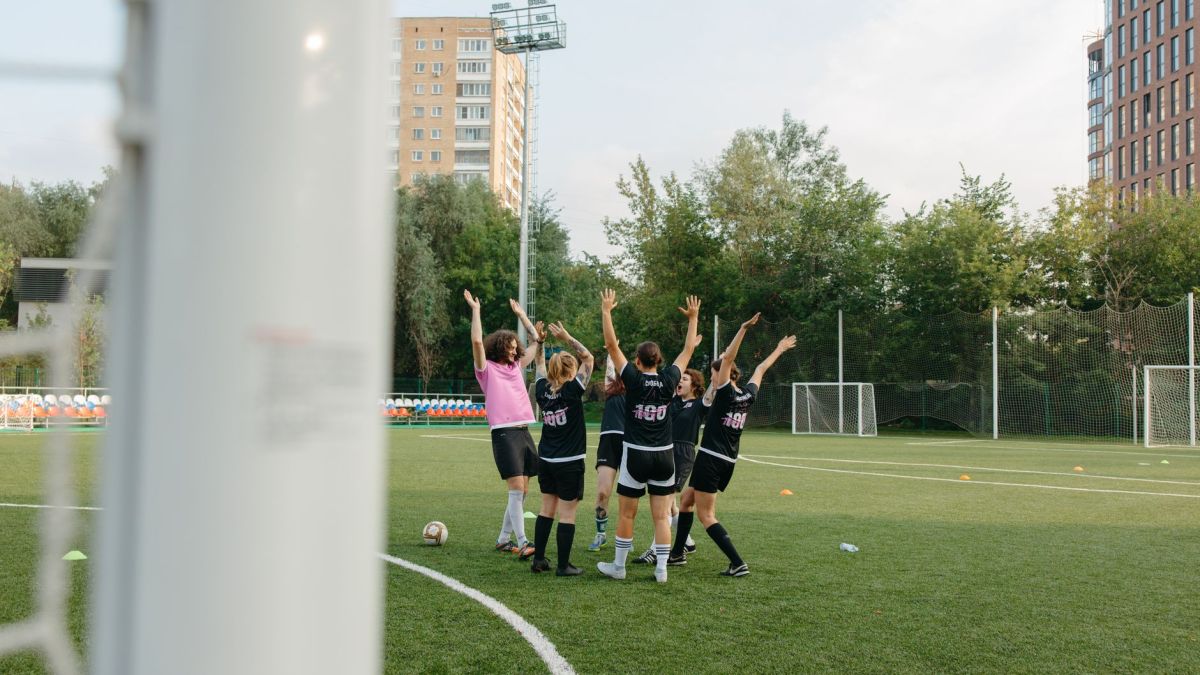 A women's soccer team in black uniforms celebrates a victory on an outdoor soccer field.