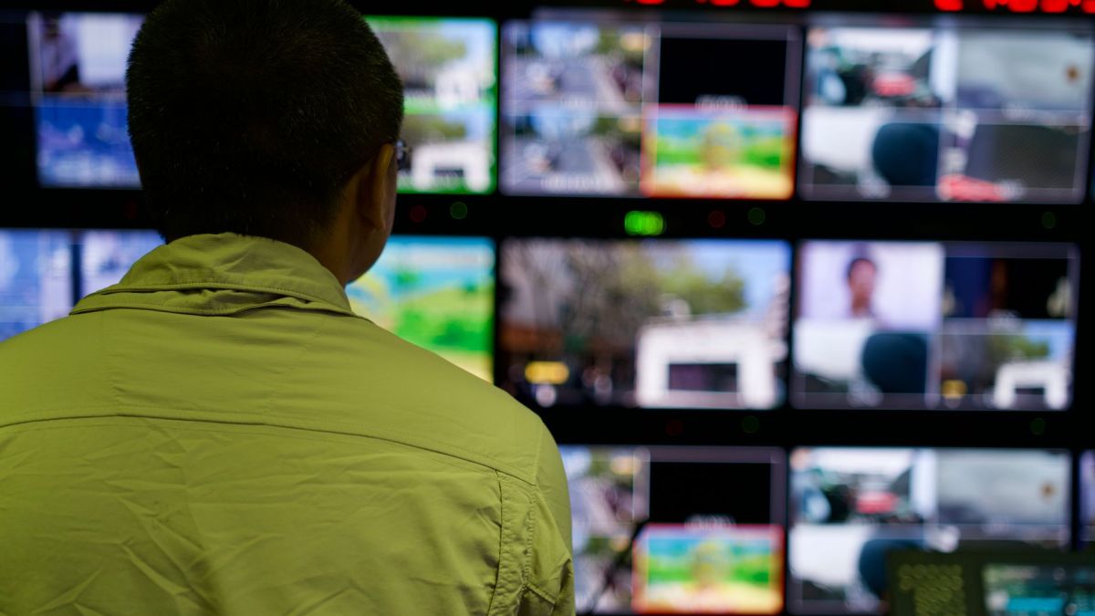 Man in a control room overseeing multiple monitors displaying various scenes.