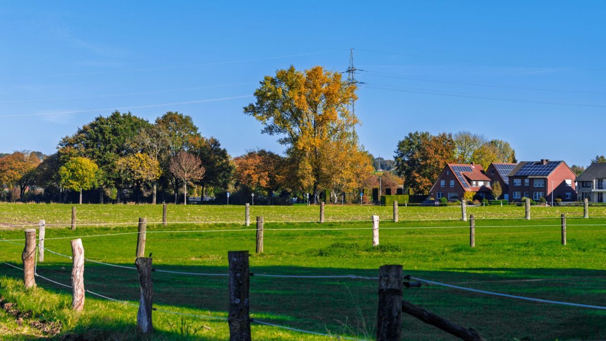 Scenic view of a rural landscape featuring green fields, trees in autumn colors, and distant houses.