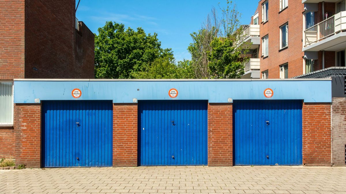 Three blue garage doors in a brick building on a sunny day.