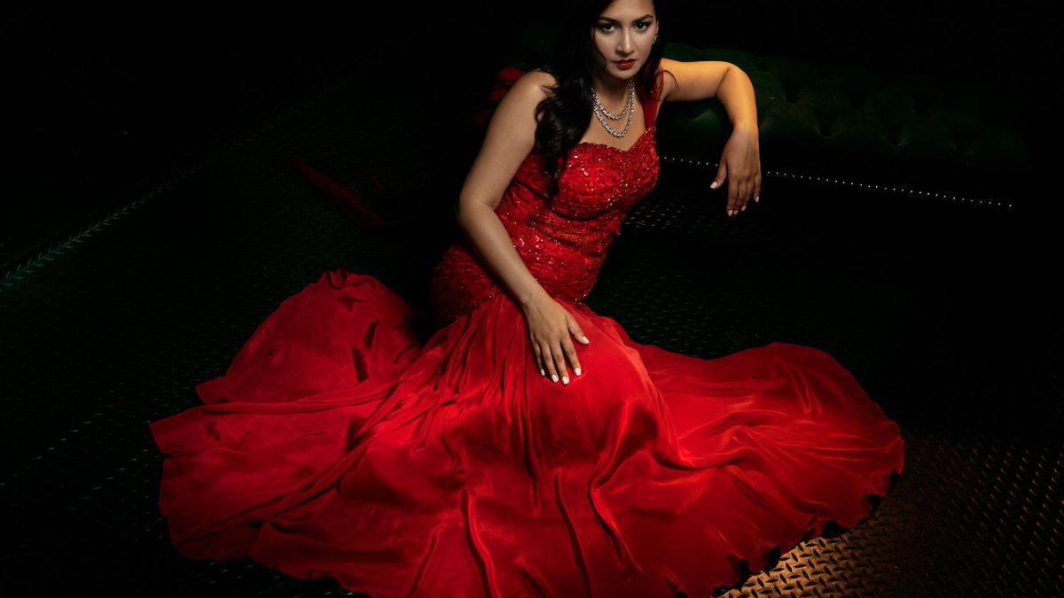 Captivating portrait of a woman in a red gown, exuding elegance and luxury against a dark backdrop.