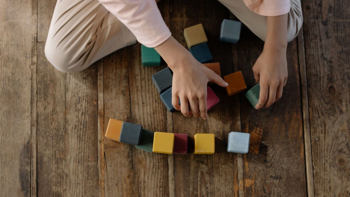 Child arranging colorful toy blocks on a wooden floor, creativity at play.