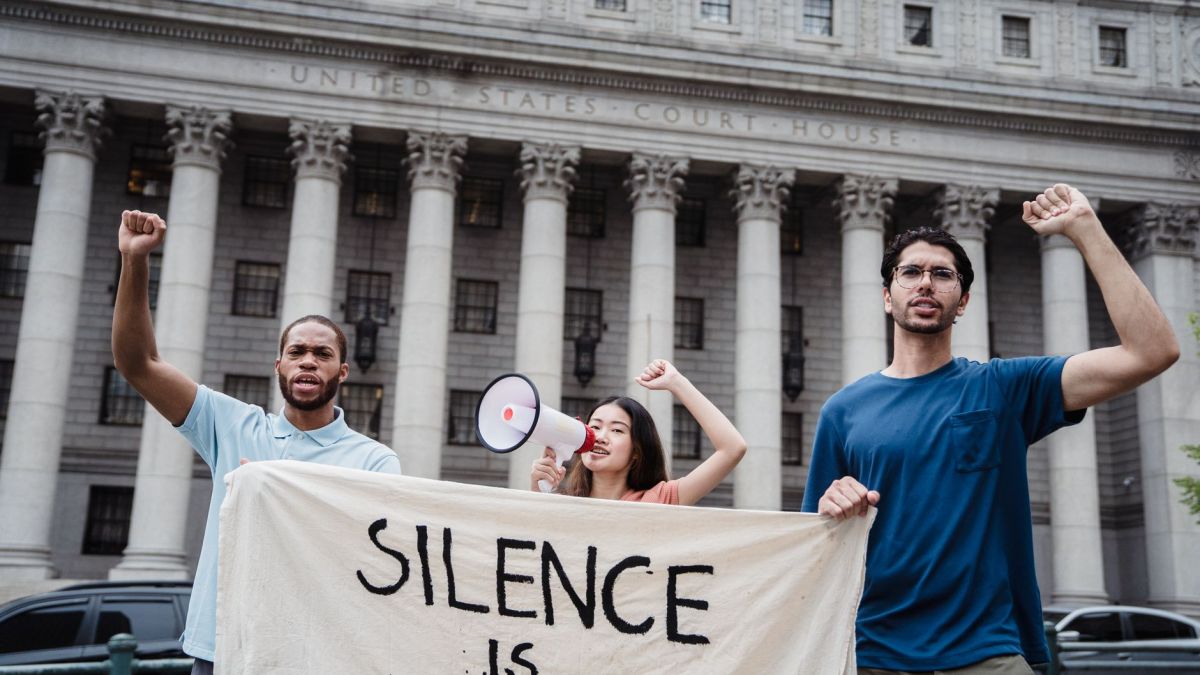 Group of diverse activists holding banner and megaphone in front of a US courthouse for a protest.