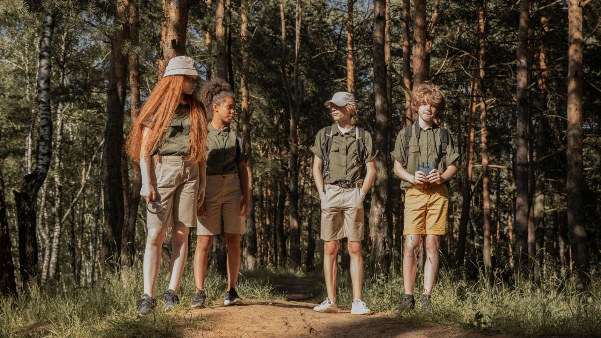 Group of teenage scouts standing on a forest trail, enjoying a sunny adventure.