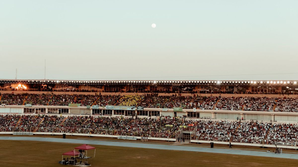 A bustling crowd fills the stadium under a clear evening sky, creating a vibrant atmosphere.