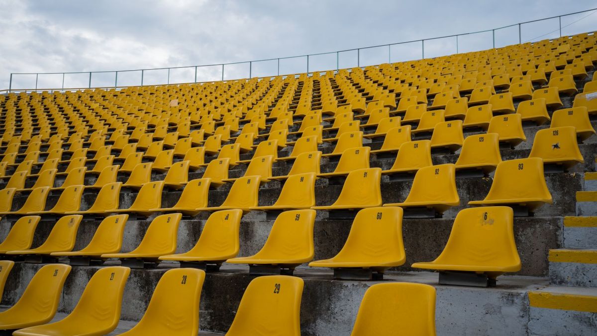 View of empty yellow seats arranged in rows at a stadium on a cloudy day.