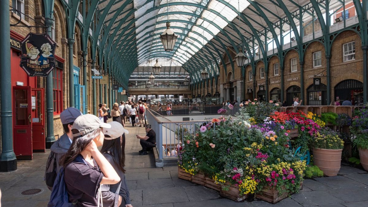 Vibrant flowers in London's iconic Covent Garden Market, busy with tourists and locals enjoying a sunny day.