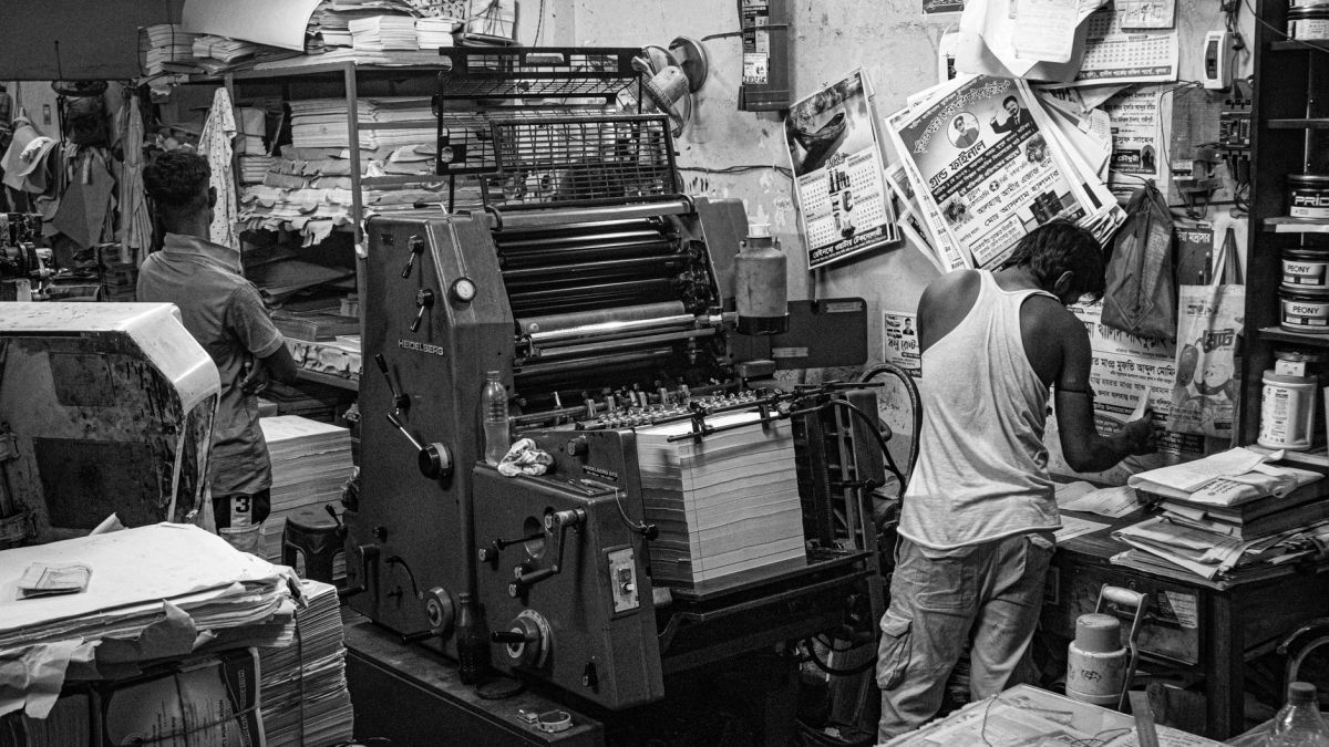 Black and white image of a bustling print shop with workers operating a printing press.