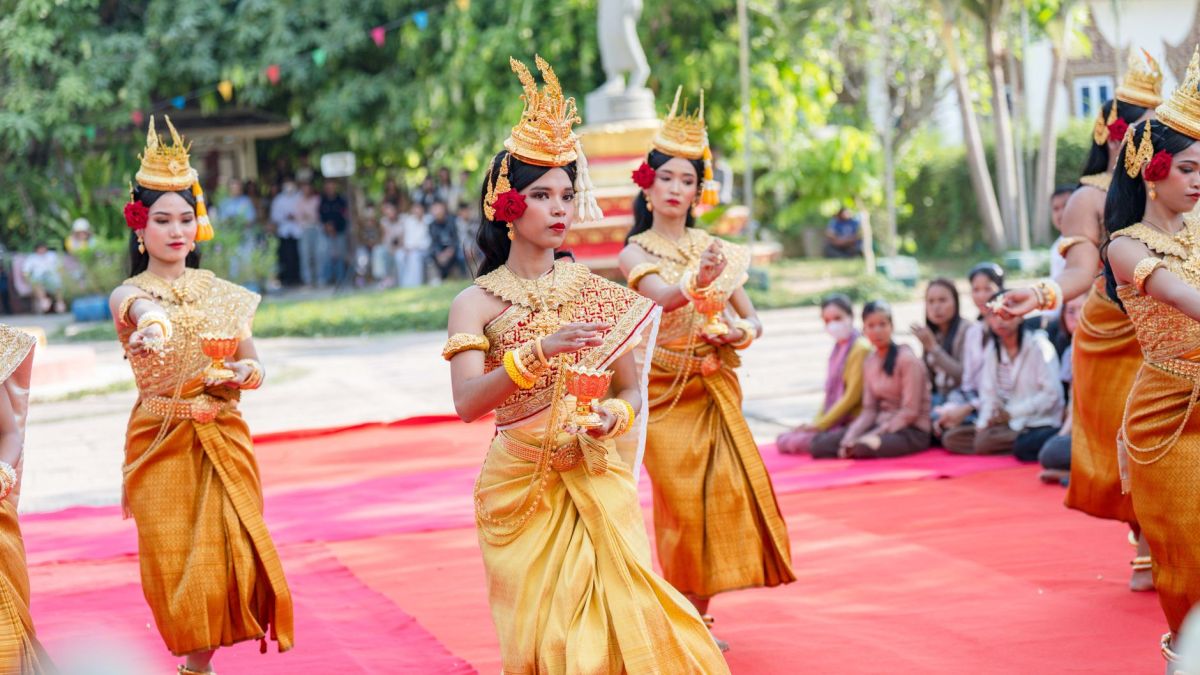 Colorful traditional Cambodian dance performance with women in elegant costumes on red carpet outdoors.