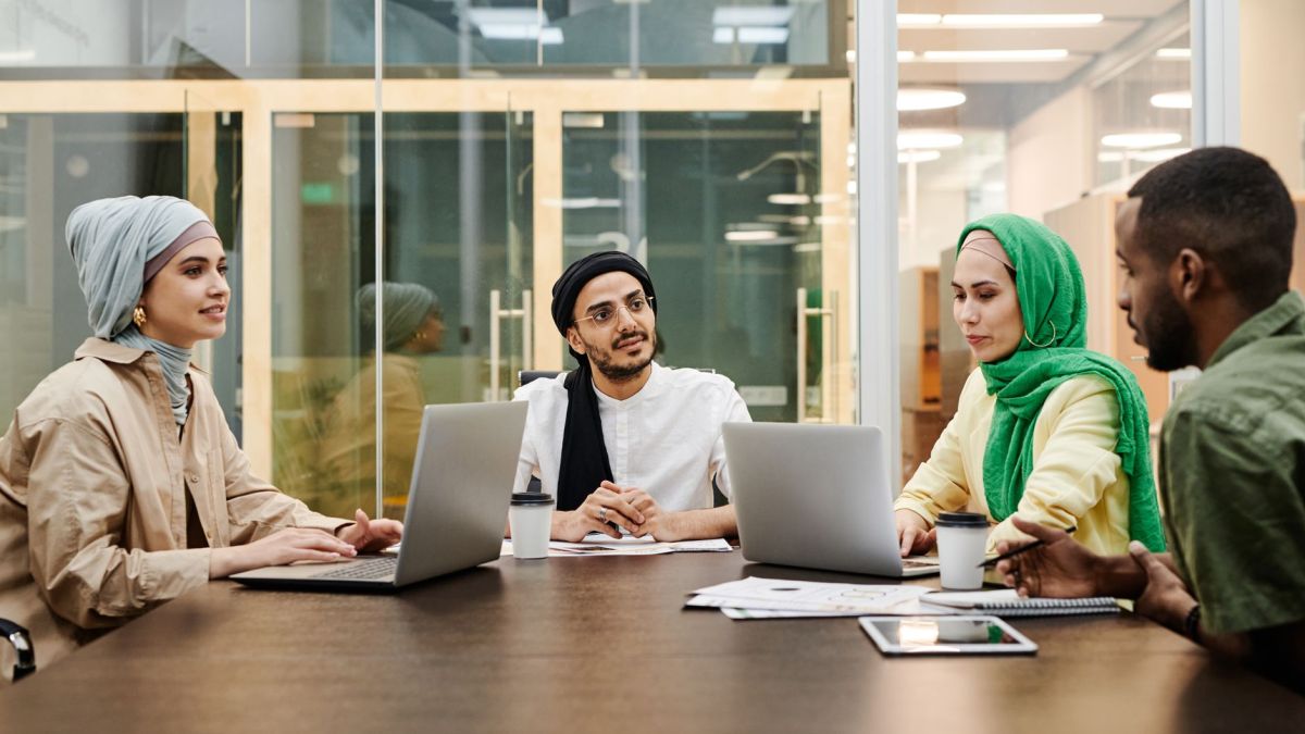 A diverse group discussing ideas in a modern office setting, using laptops and tablets.