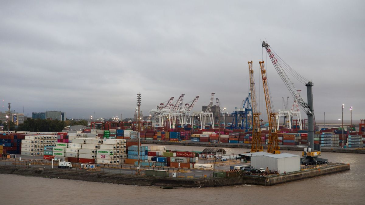 Expansive view of a busy industrial port with shipping containers and cranes under cloudy skies.