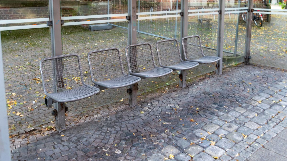 An empty bus shelter with metal mesh chairs on a cobblestone street.
