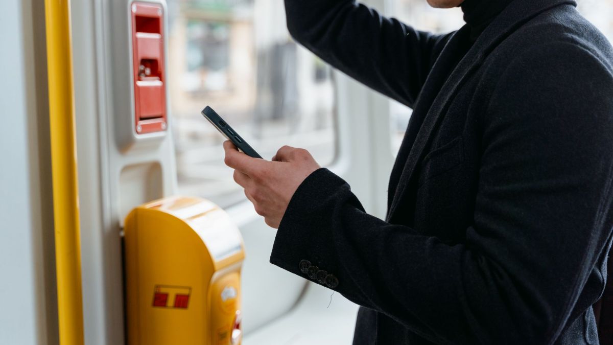 Adult in a black coat checking smartphone while commuting on public transport.