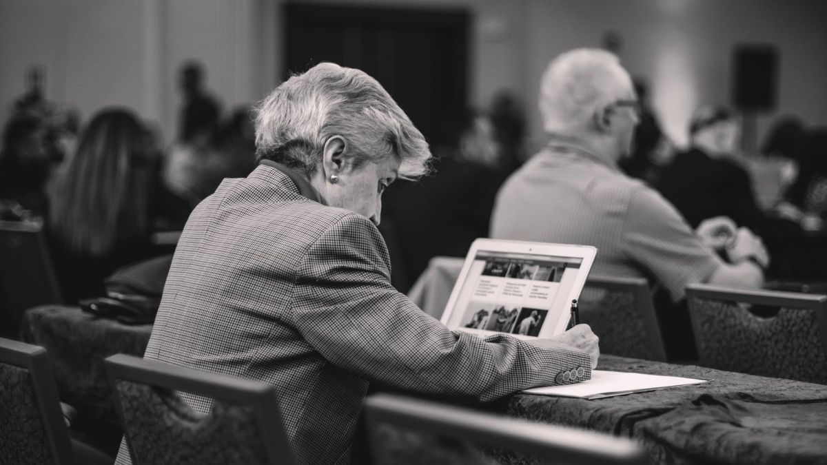 A senior journalist takes notes during a conference, engrossed in thought.