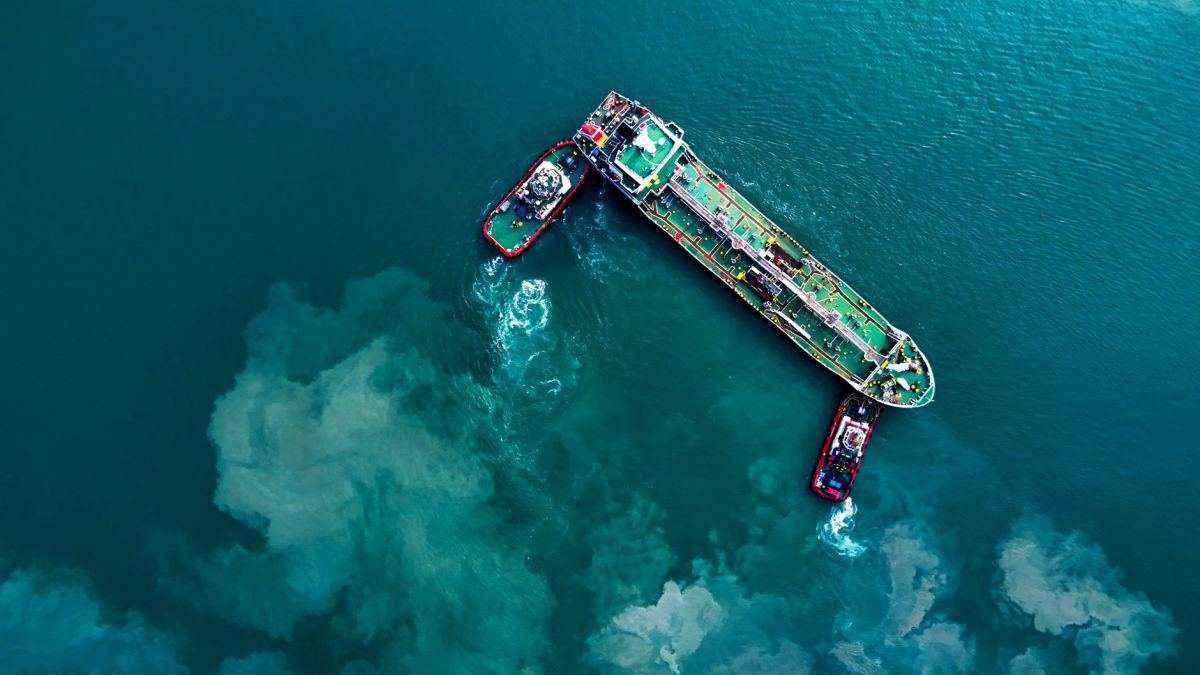 Top-down view of cargo ship and tugboats in turquoise waters near Butterworth, Malaysia.