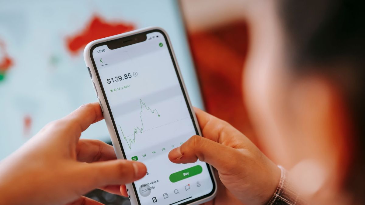 Crop anonymous trader using app on cellphone with graph and dollar price on screen in house