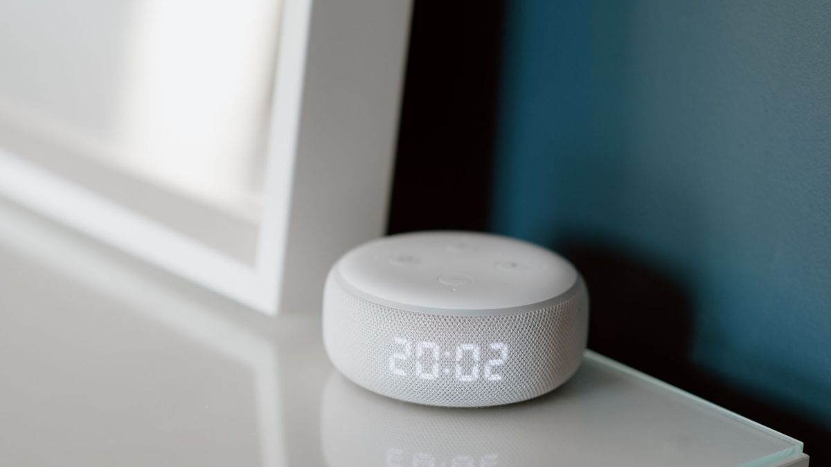 Close-up of a smart speaker with an illuminated 20:02 LED clock display on a desk.
