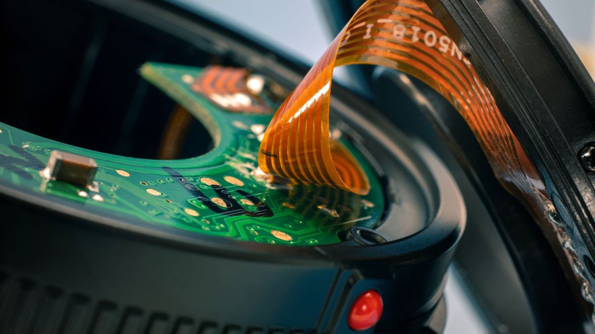 Detailed close-up of circuit board and ribbon cable in a disassembled camera lens.