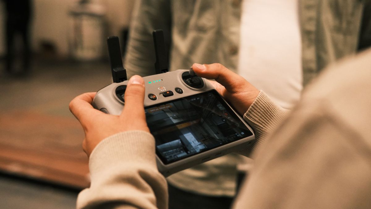 Close-up of a man using a handheld remote controller for drone operation indoors.