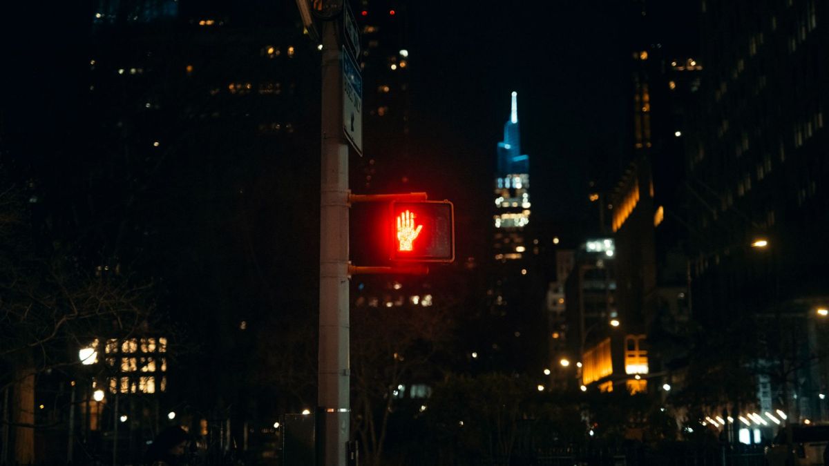 Vibrant cityscape at night with a glowing red pedestrian stop signal against skyscrapers.