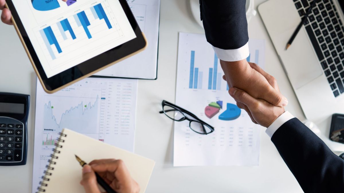 Business professionals handshake over graphs and charts in a corporate setting, symbolizing successful negotiation and agreement.