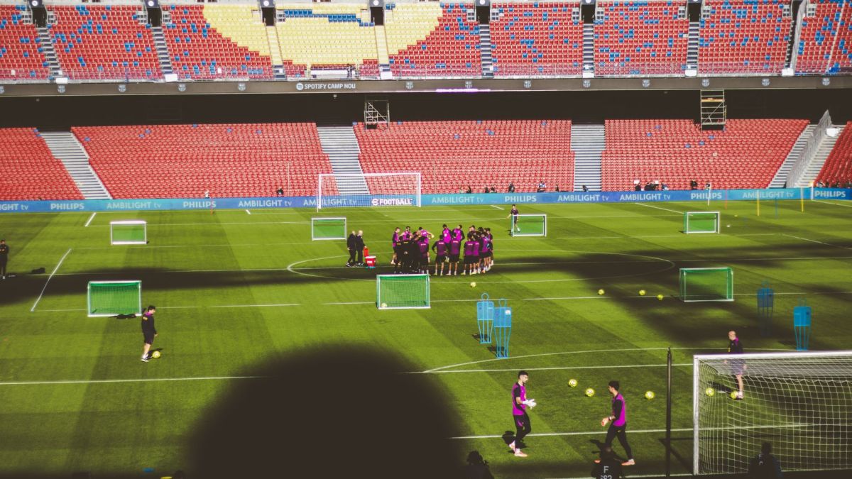 Football team training in a large empty stadium with vibrant red and blue seats.