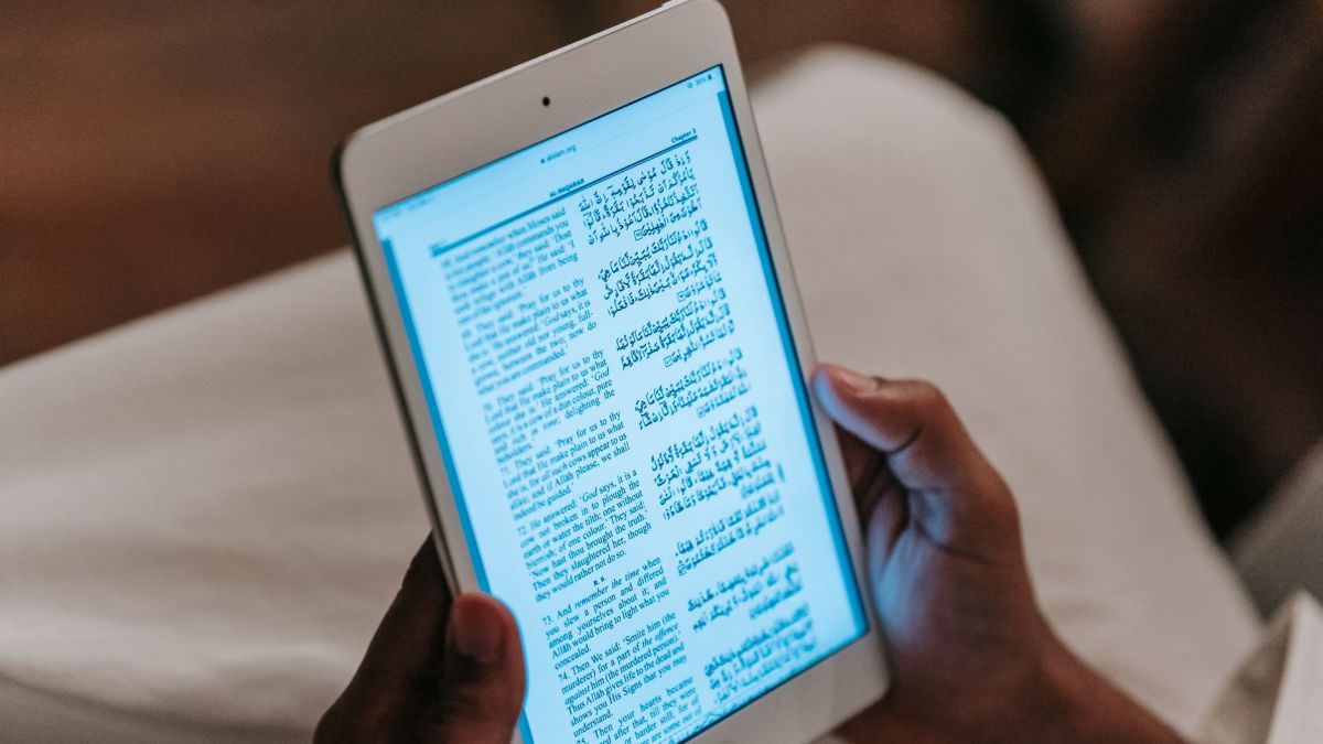 Crop unrecognizable person in casual clothes reading text on tablet against blurred background in room