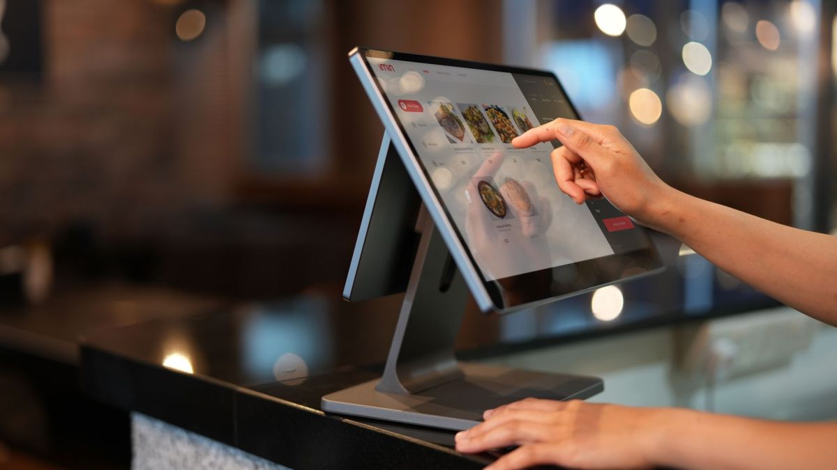 Close-up of a hand interacting with a touchscreen POS system in a restaurant setting.