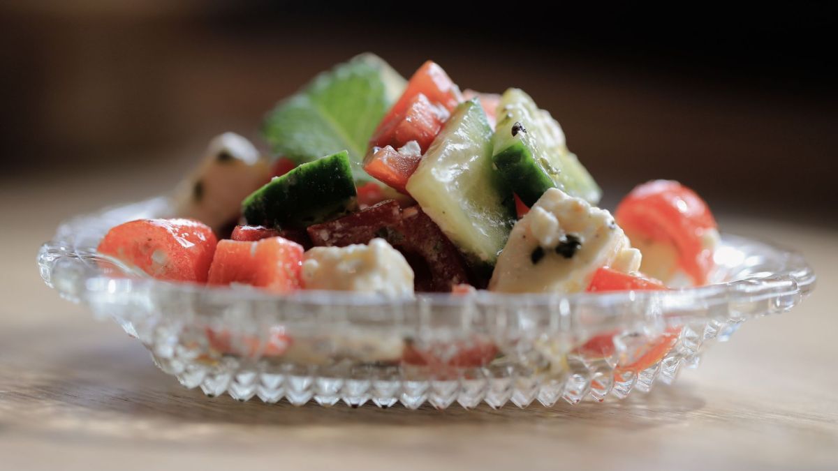 A vibrant mixed salad with feta cheese, cucumbers, and tomatoes in a glass dish.