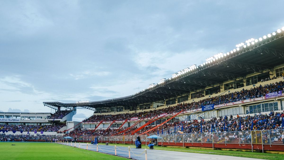 A packed stadium with enthusiastic spectators watching a live sports event under bright lights.