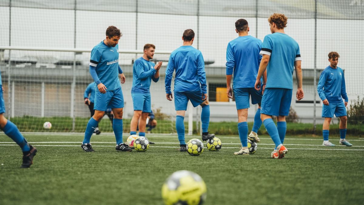 A group of soccer players in blue uniforms training outdoors on a grass field.