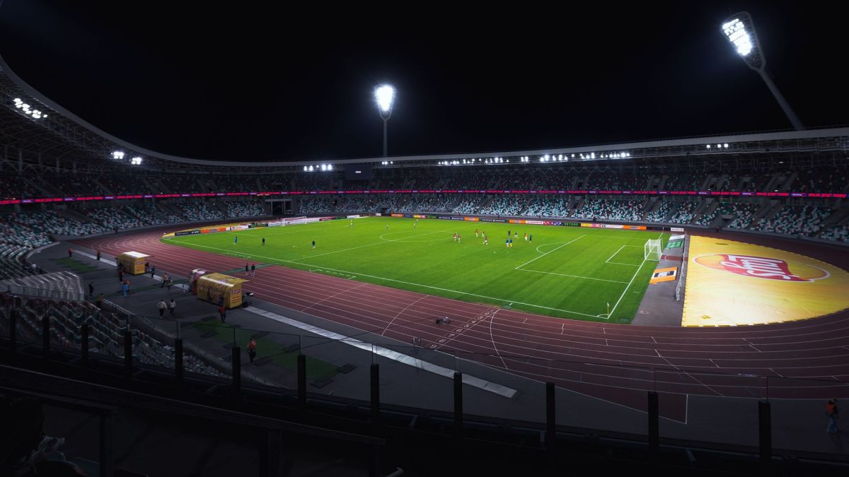 Brightly lit empty soccer stadium with green field under spotlights during night time.