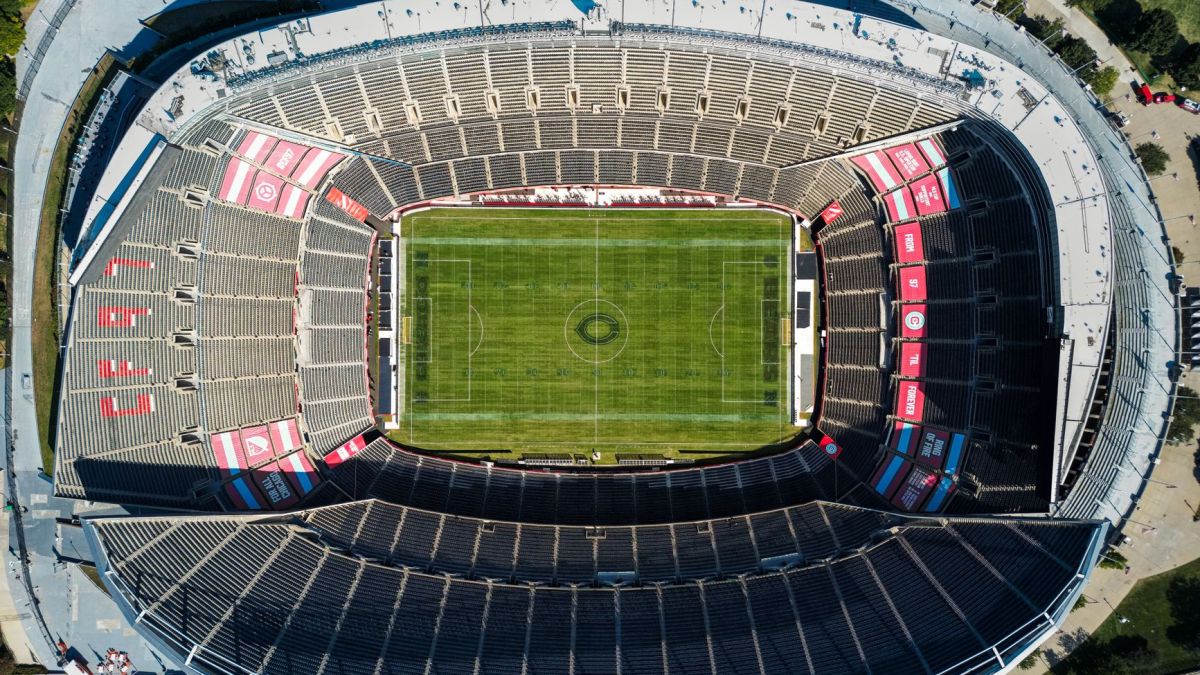 Top view of an empty soccer stadium with green field, showcasing seating arrangement under clear daylight.