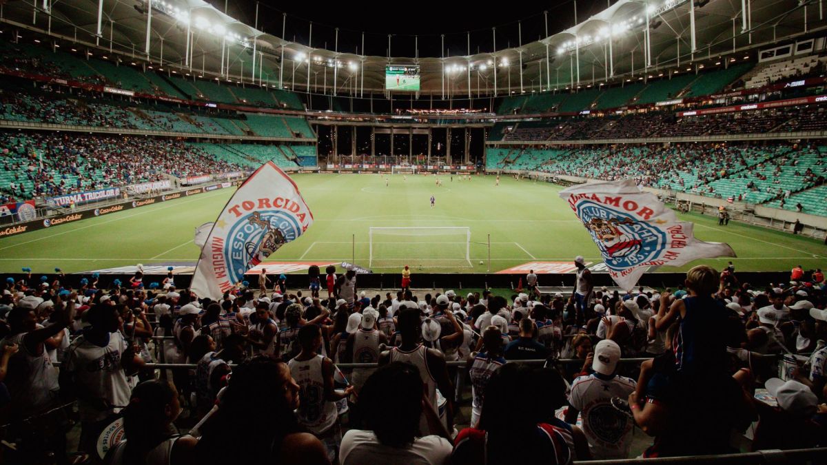 Energetic soccer fans cheer during a night match at a large stadium, creating an exciting atmosphere.