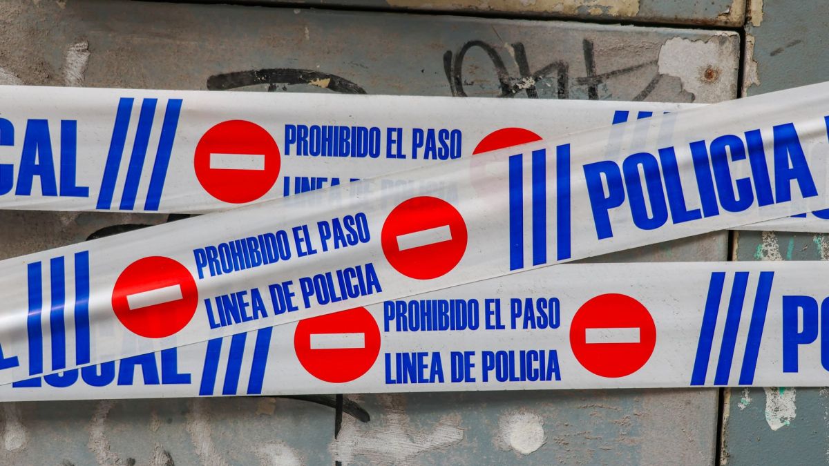 Police tape with 'Prohibido El Paso' against graffiti-covered wall. Crime scene concept.