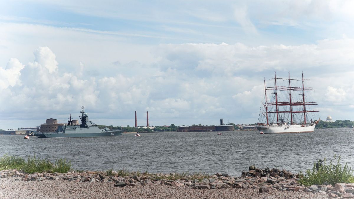 Elegant sailboat and modern warship on the river with Saint Petersburg skyline in the background.